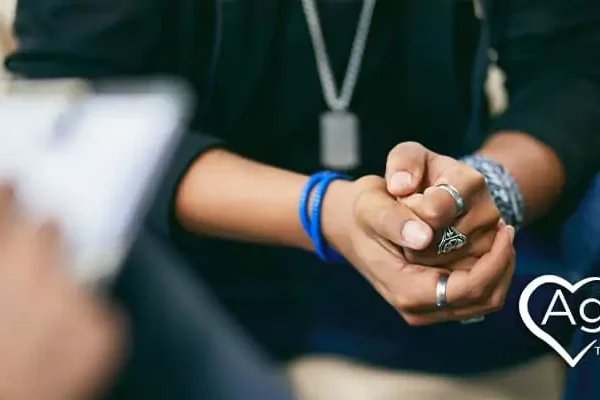 Person sitting with hands clasped, wearing jewelry and a blue wristband.