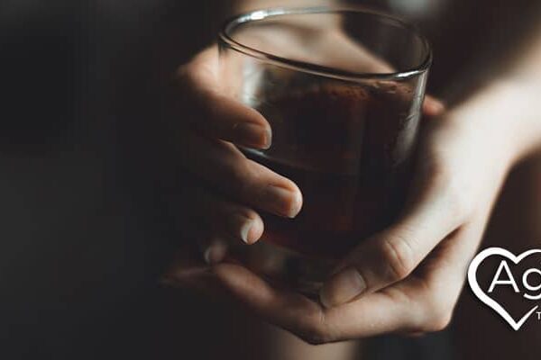 Person holding a glass of dark liquid beside Agape Treatment Center logo with heart design.