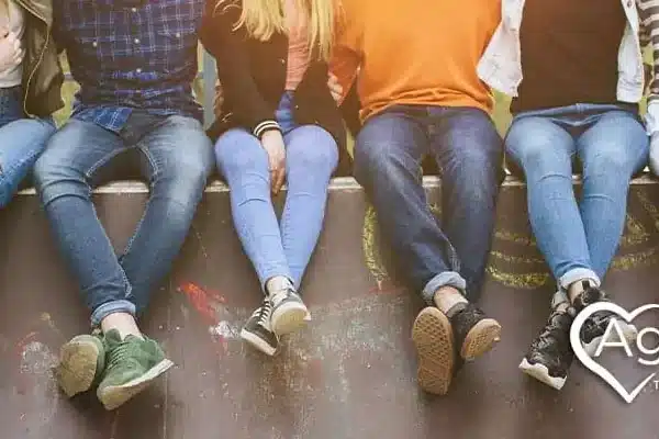 People sitting on a ledge wearing casual jeans, sneakers, and colorful tops.
