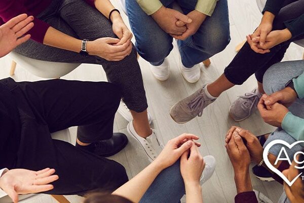 Group of people sitting in a circle, some with hands on laps, next to Agape Treatment Center logo.