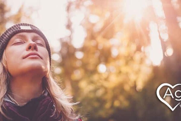 Person wearing a beanie and closed eyes in sunlight, with Agape Treatment Center logo in corner.