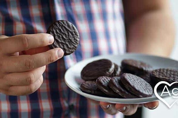 Person holding a plate of chocolate cookies wearing a checkered shirt.
