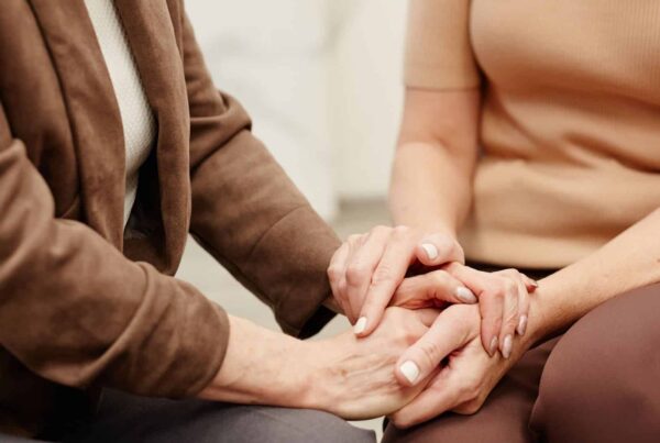 Two people sitting, wearing brown clothes, holding hands.