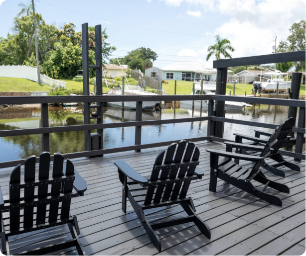 Wooden deck with black chairs overlooking a canal with boats and houses in the background.